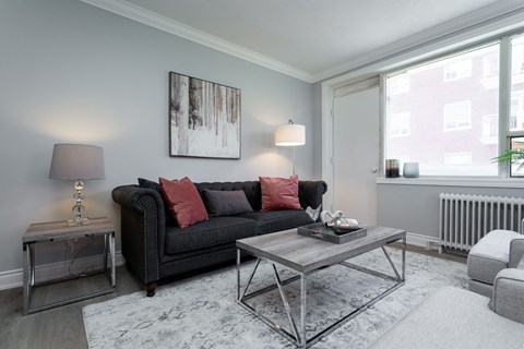 A living room with a black couch, a grey coffee table, and a large painting on the wall.