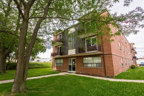 A red brick house with a balcony and a tree in front.