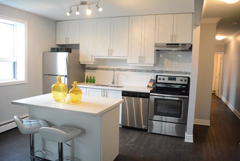 A kitchen with white cabinets and a white island with two yellow bottles on it.