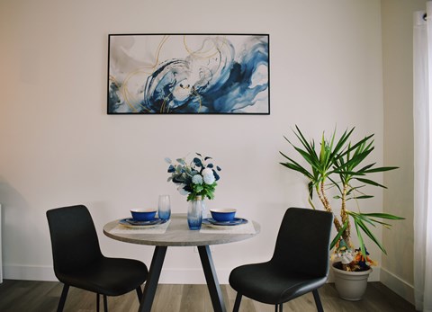 A dining room with a table set for two and a large abstract painting on the wall.