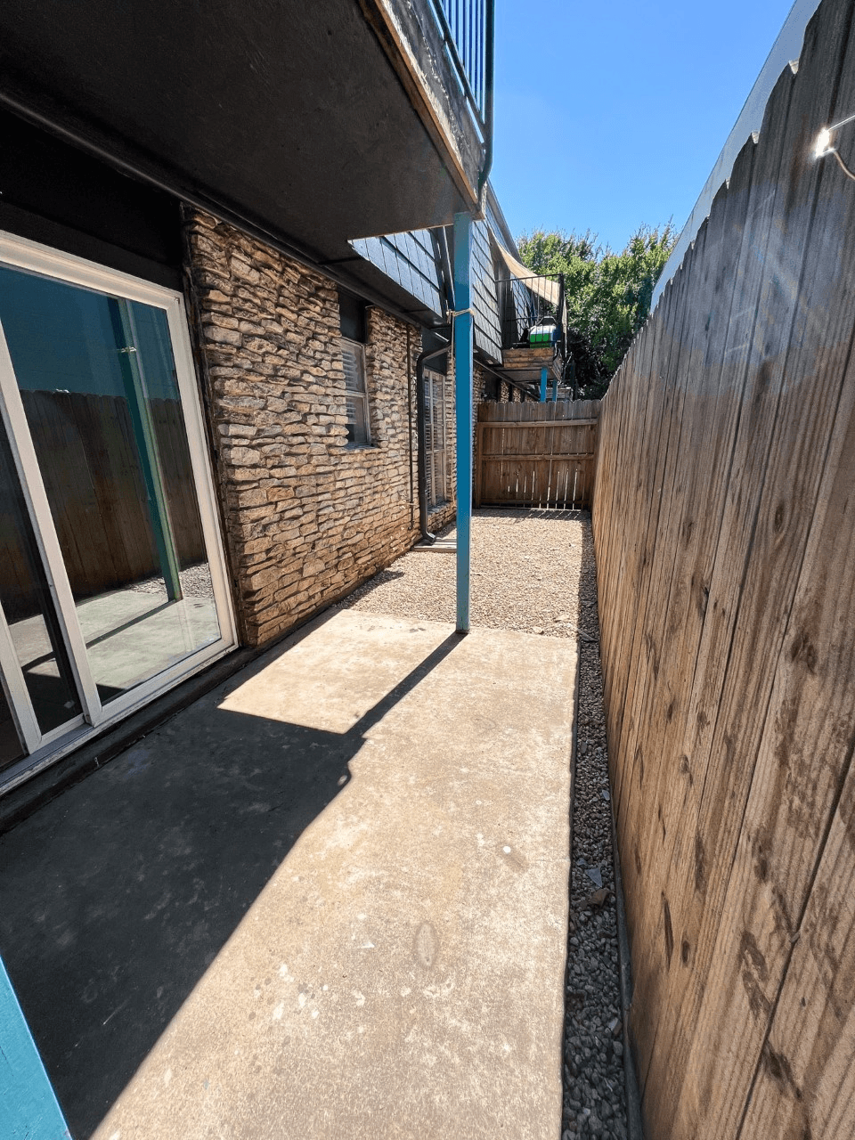 a patio with a wooden fence and a blue pole in front of a brick building