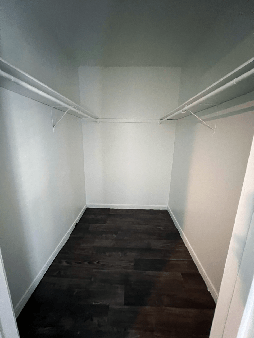 a small walk in closet with white walls and a dark wood floor