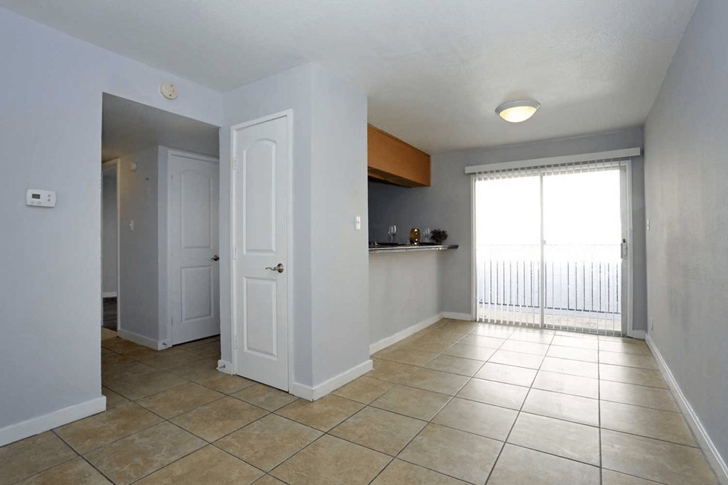 a large living room with tiled flooring and a sliding glass door leading to a balcony