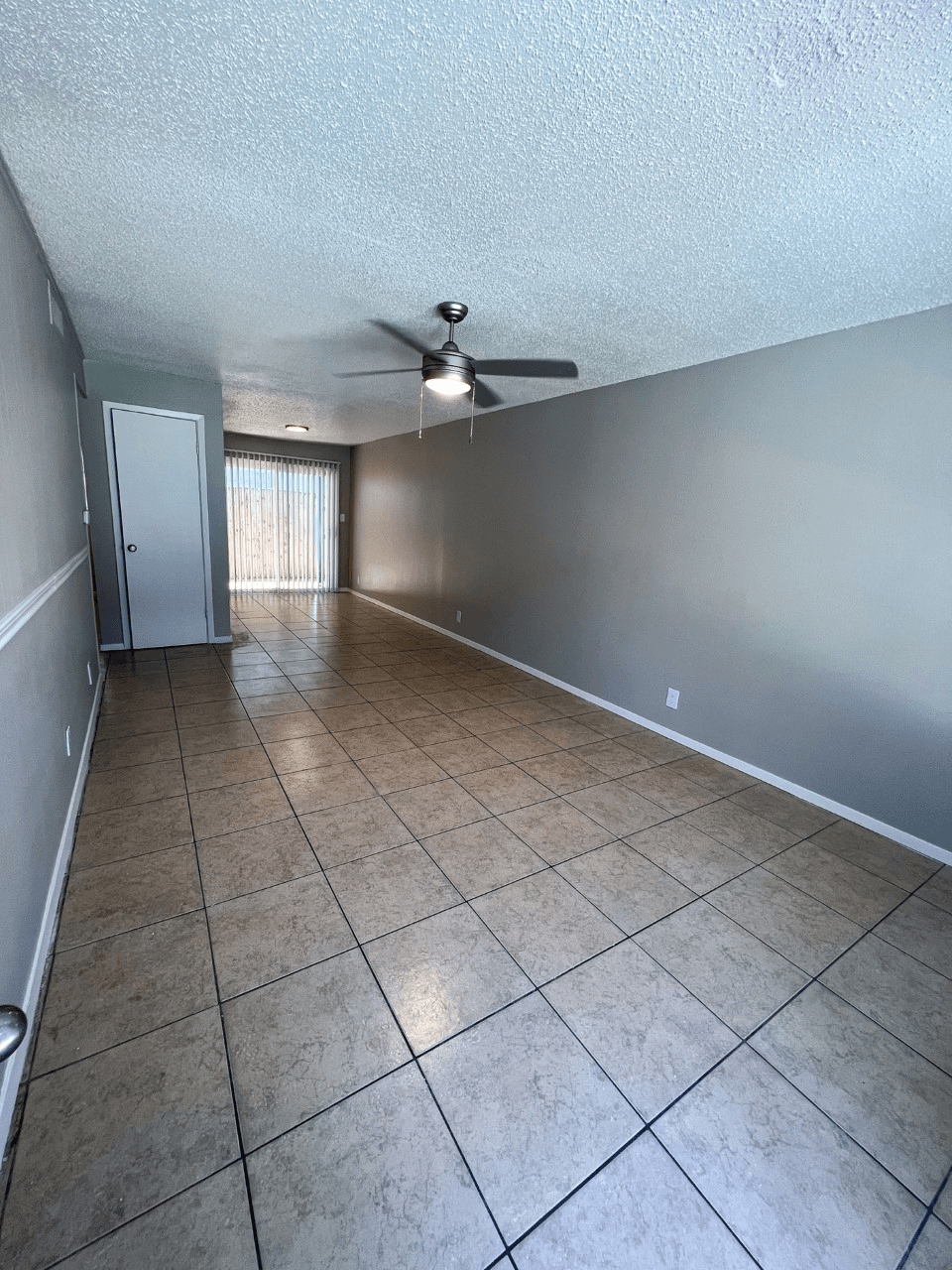 an empty living room with a ceiling fan and tiled floor