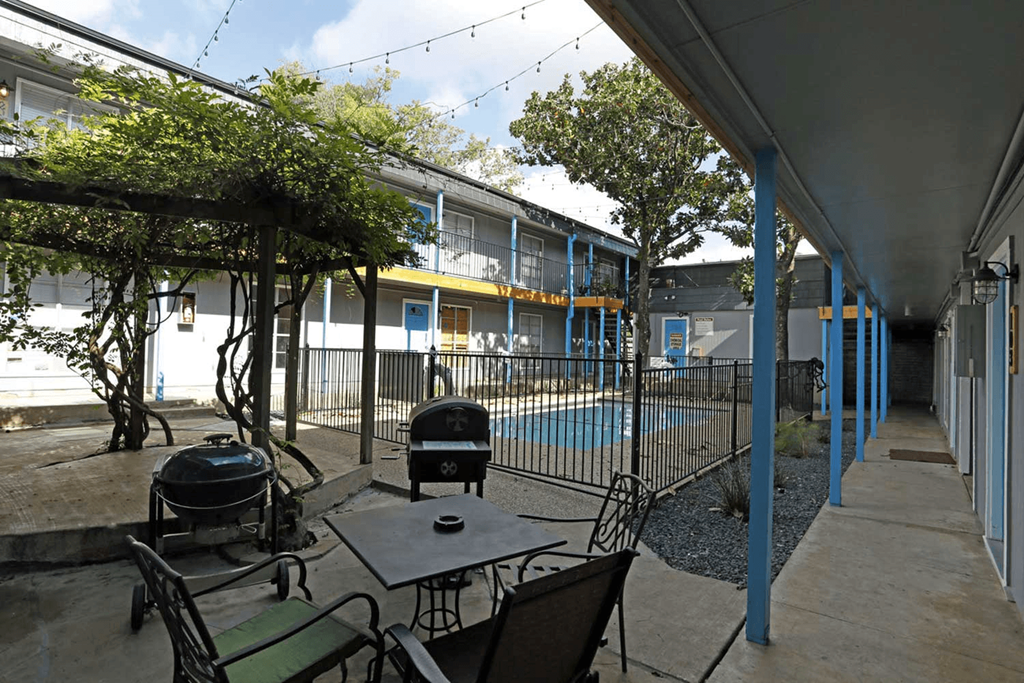 a patio with a table and chairs and a grill and a swimming pool in the background