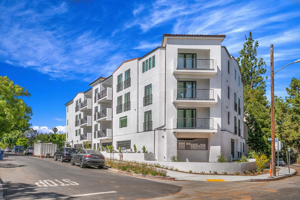 a white apartment building on a street corner with a blue sky in the background