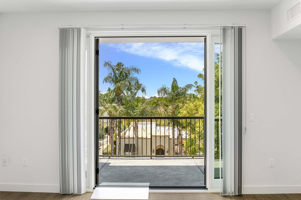 an open door leading to a balcony with trees and a building in the distance