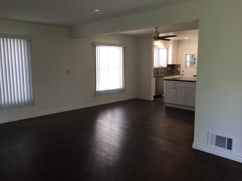 an empty living room with a kitchen in the background