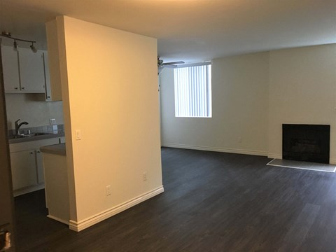 an empty living room with a fireplace and a kitchen in the background