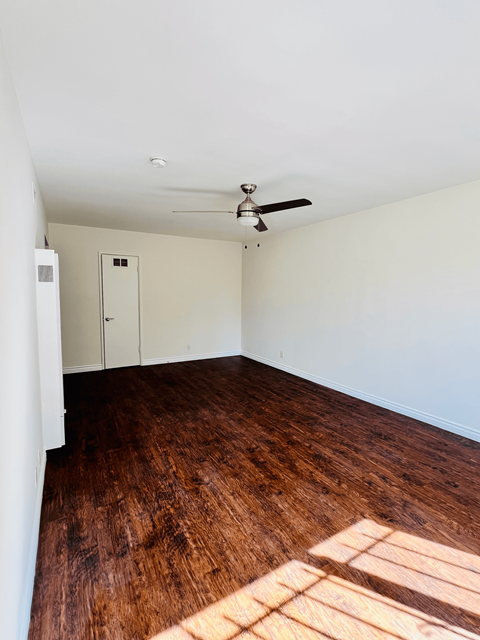 an empty living room with wood floors and a ceiling fan