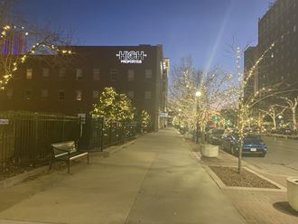 a city sidewalk with trees and a building at night