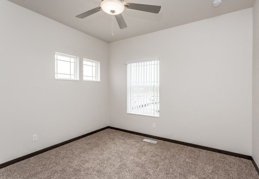 an empty room with a ceiling fan and two windows