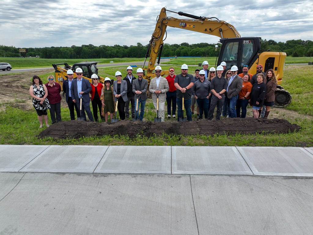 a group of people standing in front of a mound of dirt with a tractor behind