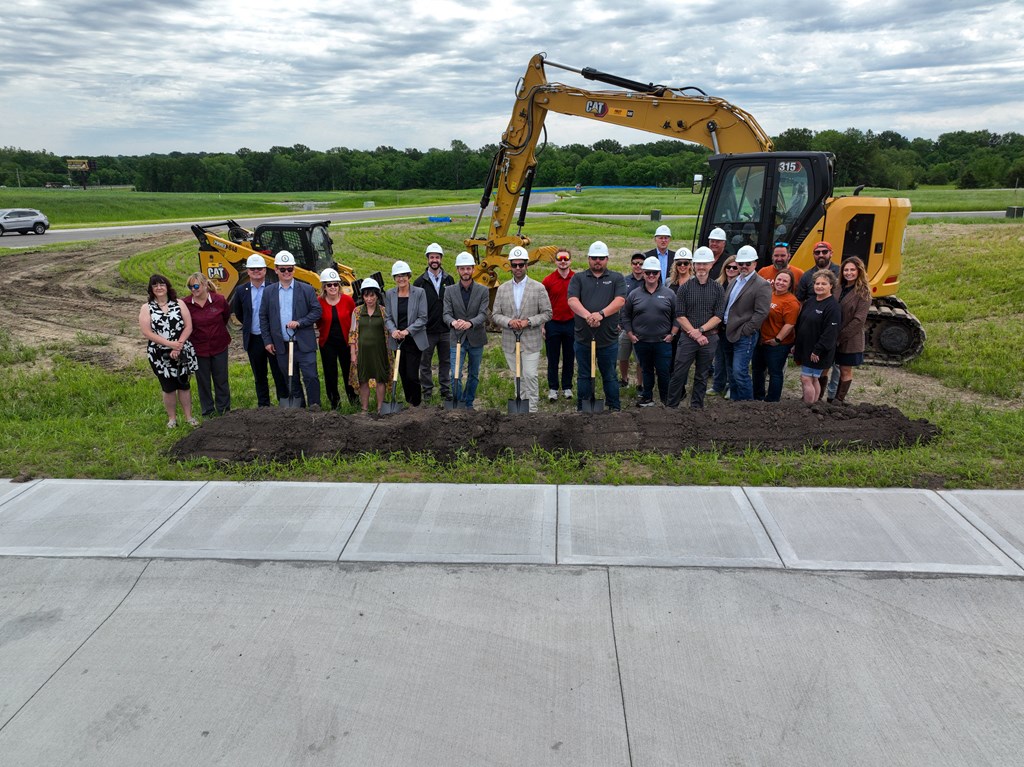 a group of people standing in front of a mound of dirt with a tractor behind