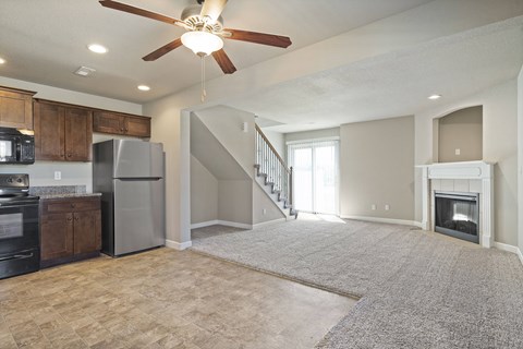 an empty living room with a kitchen and a ceiling fan