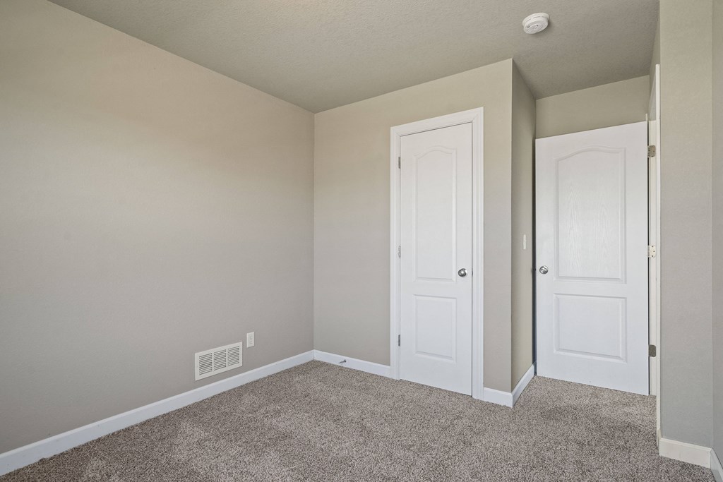 an empty bedroom with two doors and a carpeted floor