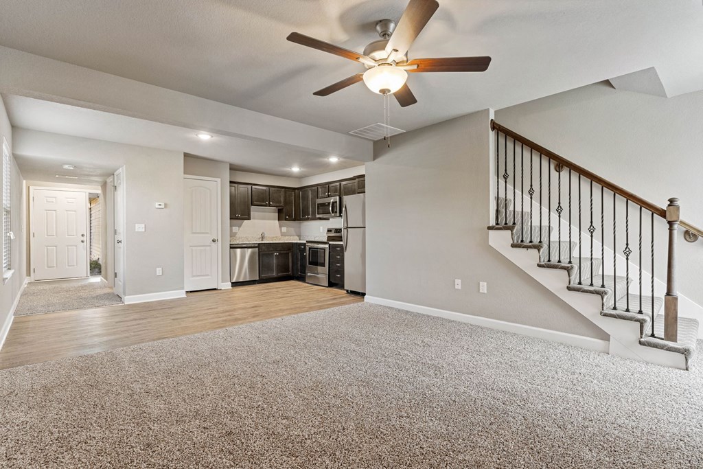 an empty living room with a ceiling fan and a kitchen