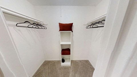 a walk in closet with a white shelving unit and a red cushion on top of it