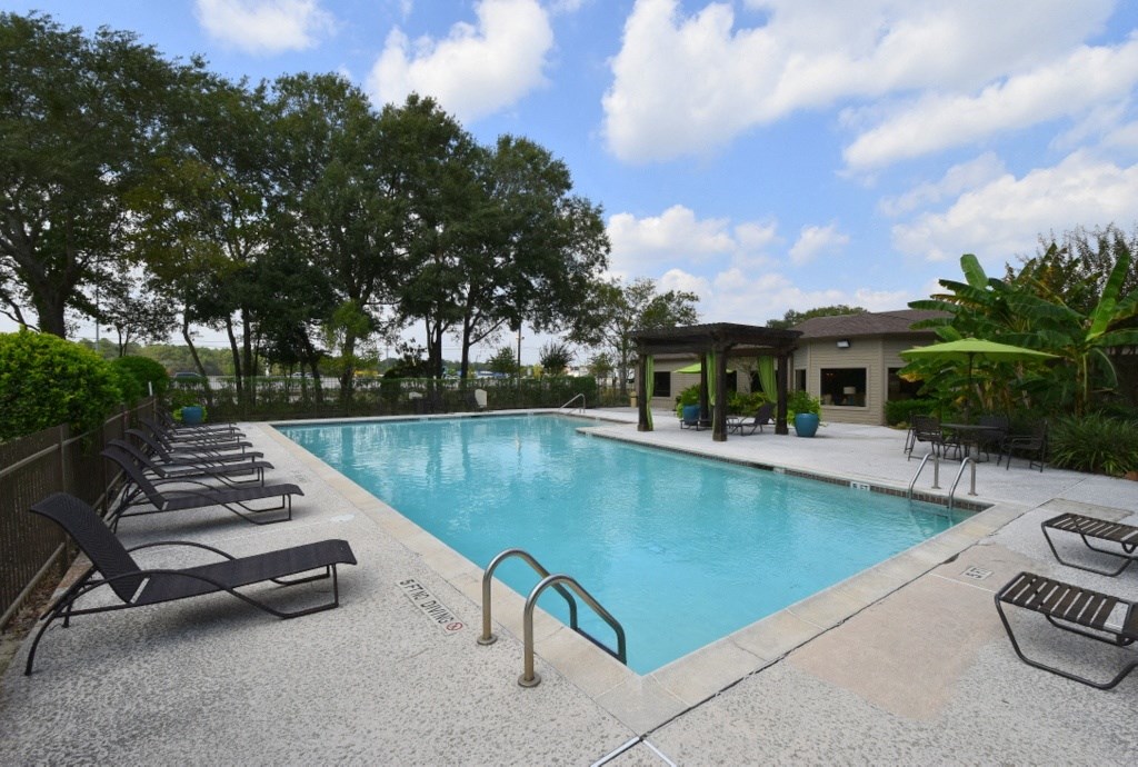 a swimming pool with chaise lounge chairs and trees in the background