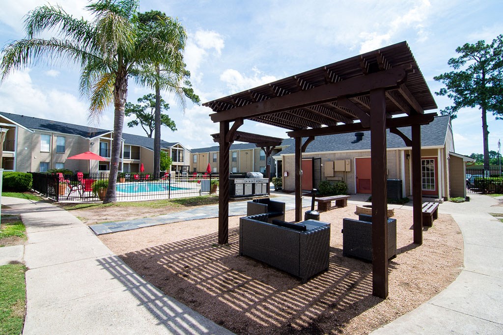 a pergola sits in front of a swimming pool with a pool house in the background