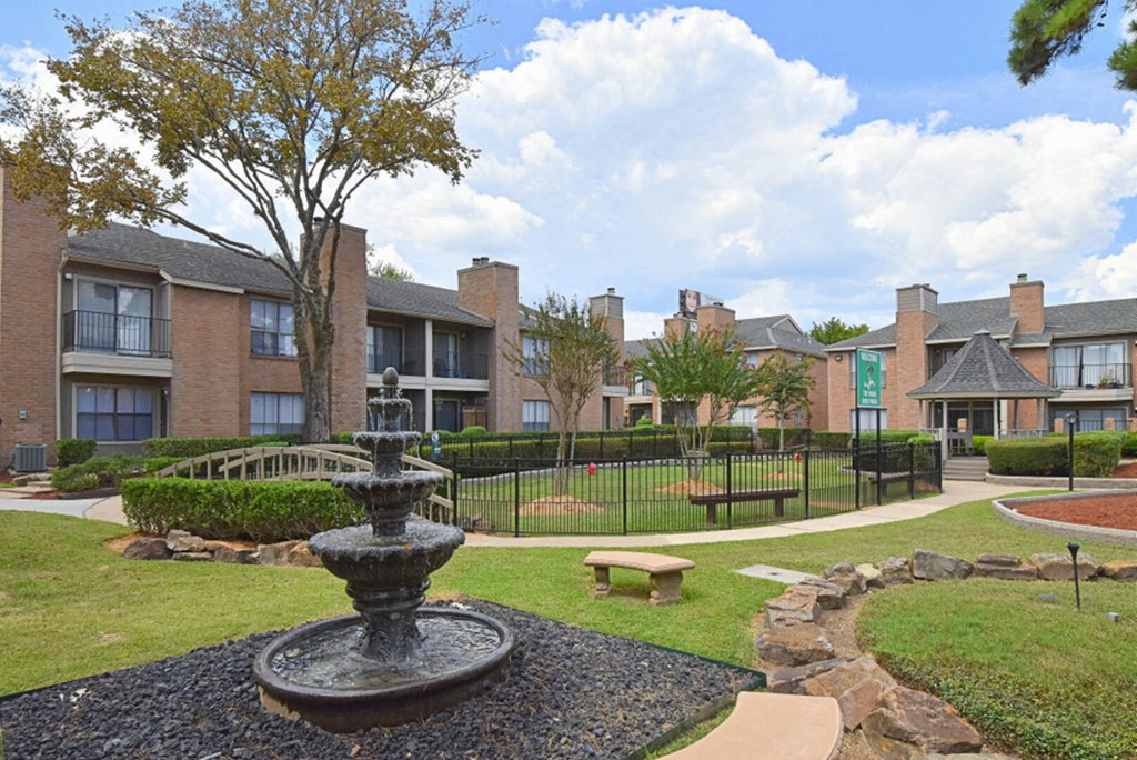 a fountain sits in the middle of a grassy area in front of an apartment complex
