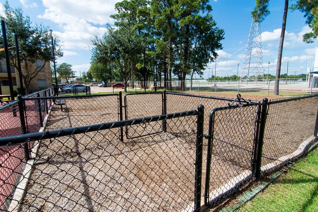 a fenced in baseball field with trees and a parking lot in the background