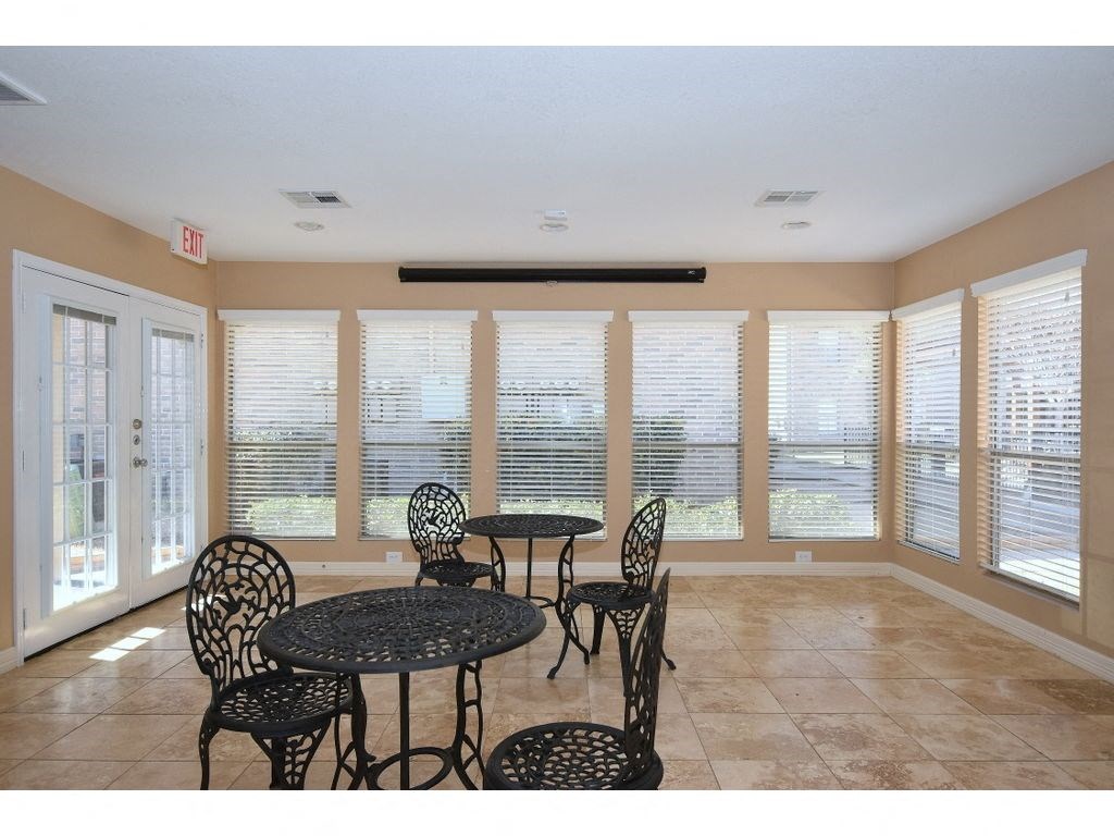 a room with a table and chairs and a large window with blinds