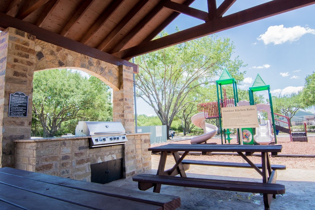 a picnic table with a grill and playground in the background