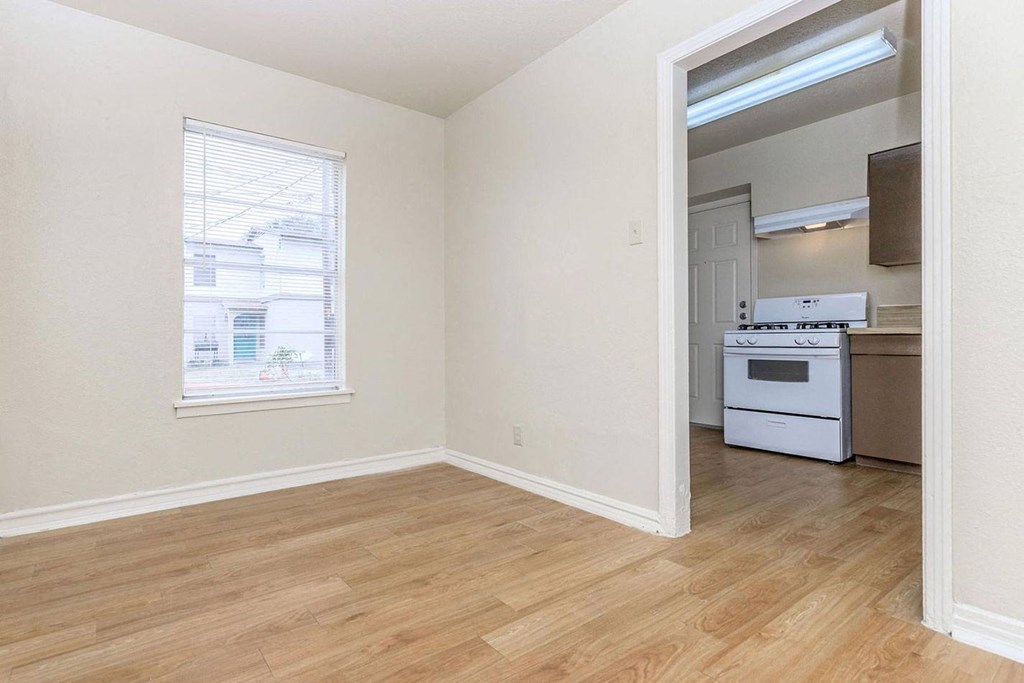 an empty room with a window and a kitchen in the background