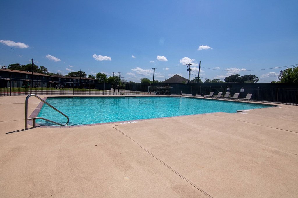 a large swimming pool with chairs around it and a blue sky in the background