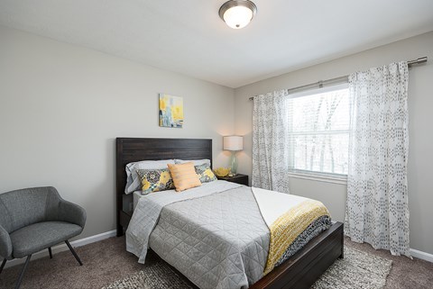 A bedroom with a bed, chair, and window.