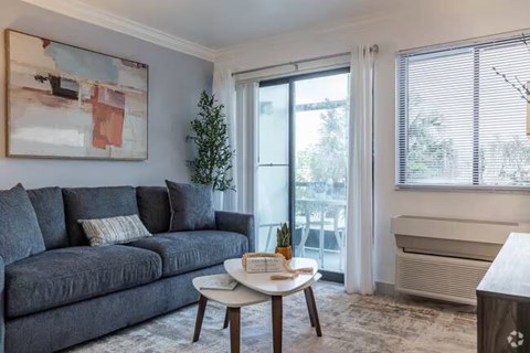 A living room with a grey couch, a small table with a plant on it, and a painting on the wall.