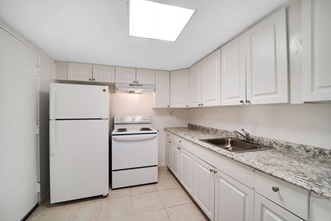 A white kitchen with a refrigerator, stove, and sink.