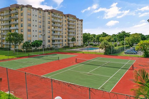 A tennis court is surrounded by a fence and apartment buildings.