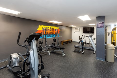 A gym with a variety of equipment including a treadmill, a bench, and a television.