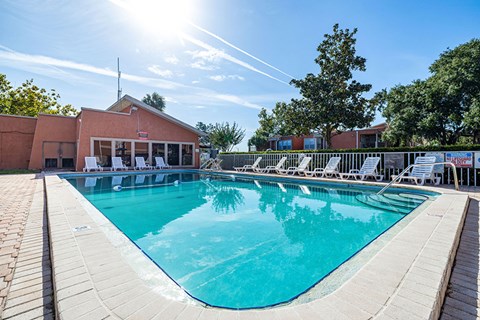 A large outdoor swimming pool with sun loungers and a building in the background.