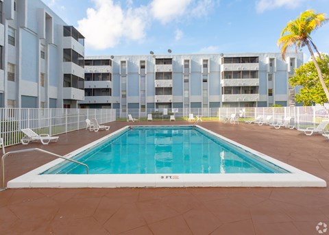 A large outdoor pool surrounded by a fence and chairs.