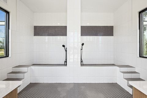 A modern bathroom with a large white tub and two black shower heads.