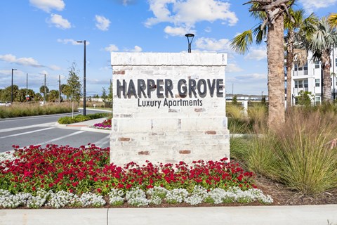 A sign for Harper Grove Luxury Apartments is surrounded by flowers.