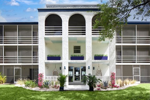 the front of a white building with a lawn and plants