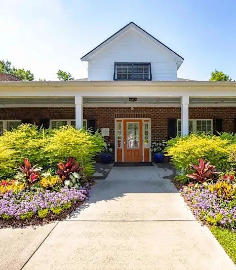 A white house with a brown door and windows surrounded by a garden.