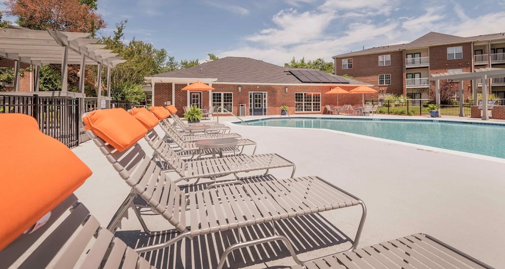 A pool surrounded by orange sun loungers and a building in the background.