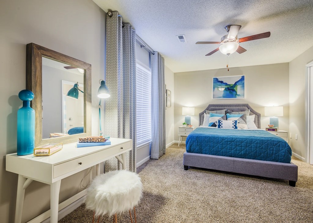 A bedroom with a blue bed and a white desk with a mirror.