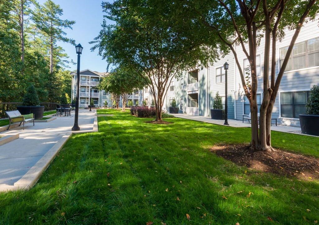 a courtyard with green grass and trees in front of a building