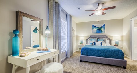 A bedroom with a blue bedspread and a white dresser with a mirror.