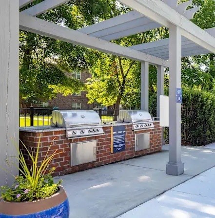 A white pergola is over a brick wall with three grills under it.