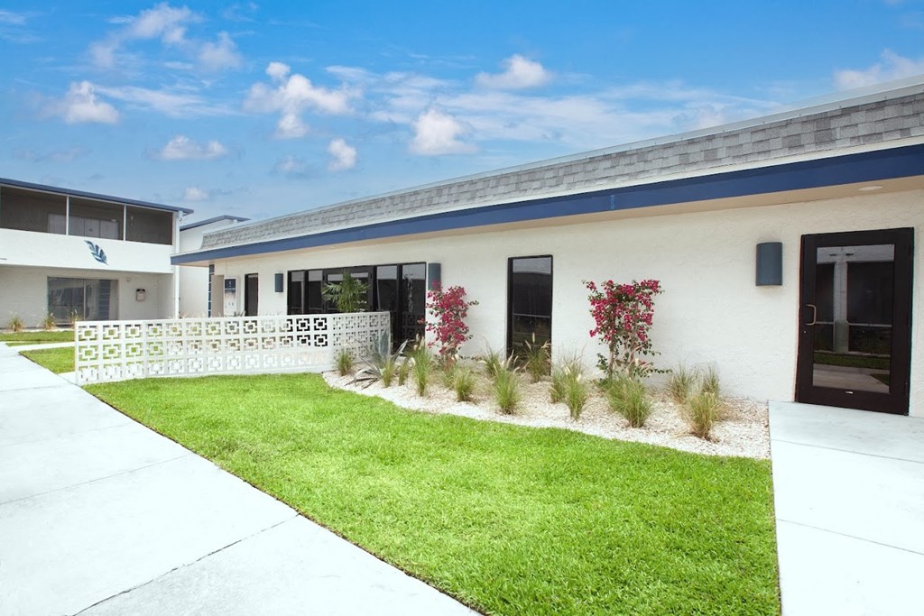 the front of a white building with a lawn and grass
