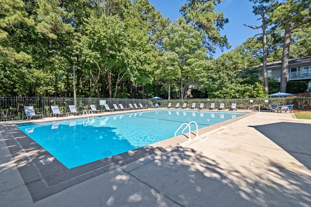 a swimming pool with chairs around it and trees in the background