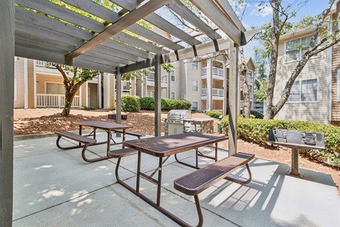 two picnic tables with benches under a pergola in front of an apartment building