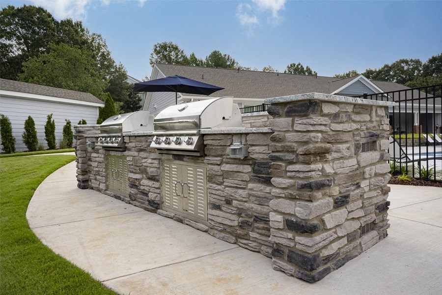 a stone outdoor kitchen with a grill on the side of a driveway